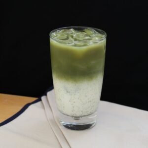 Refreshing iced matcha latte in a glass with milk on a wooden table.