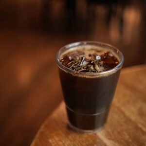 Close-up of a cold brew coffee with ice cubes in a plastic cup on a wooden table indoors.