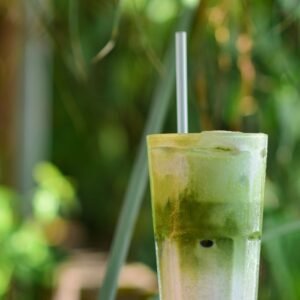 A chilled glass of iced matcha latte with a straw in a natural outdoor setting, perfect for summer.
