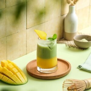 Iced mango matcha drink with fresh mint, sliced mango, and matcha powder in a cozy kitchen setting.