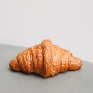 A delicious golden croissant photographed on a minimalist surface, perfect for breakfast themes.